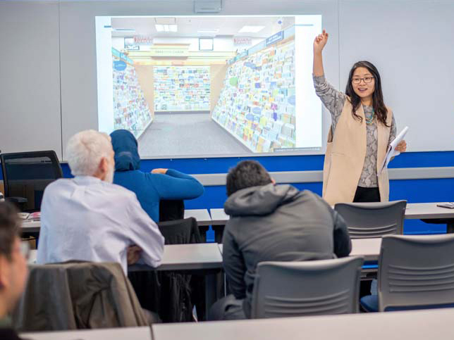 A professor lectures in front of students taking notes.