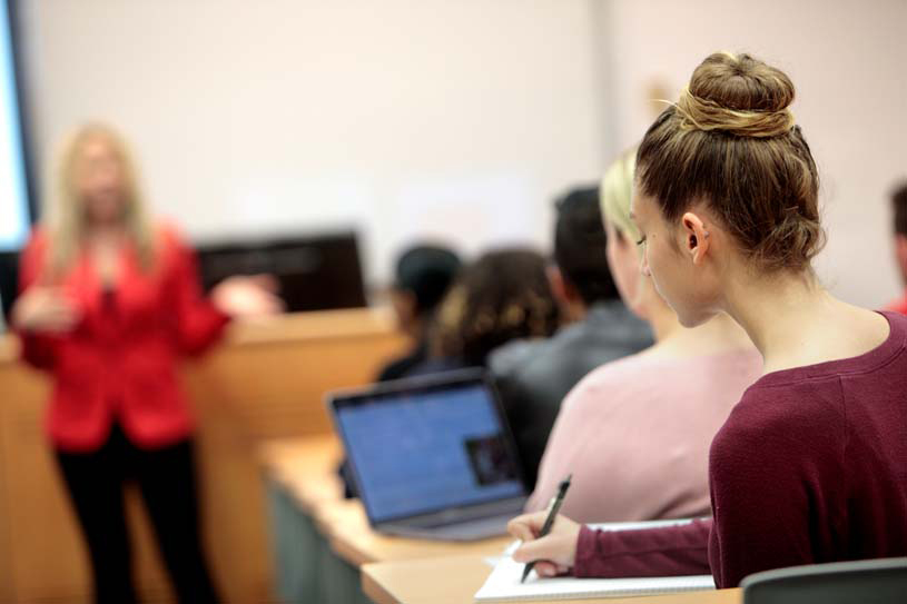 A student writing in a notebook during a classroom lecture