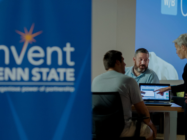 three people at a laptop with an invent penn state banner in foreground