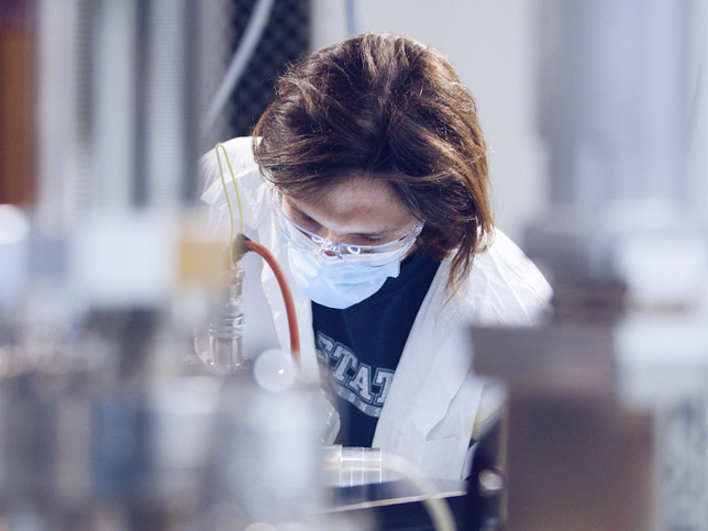 Masked student in white coat in research lab